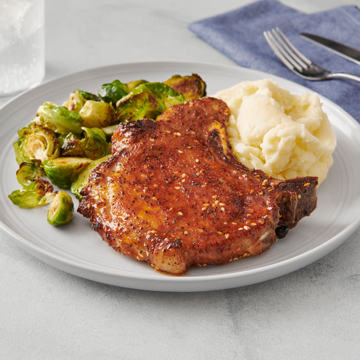 A plate of food with a pork chop mashed potatoes and Brussels sprouts.