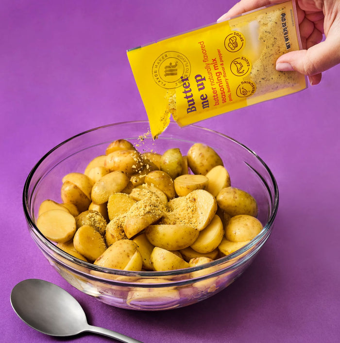 A hand pours Go Wise seasoning onto a bowl of halved potatoes ready to be cooked.