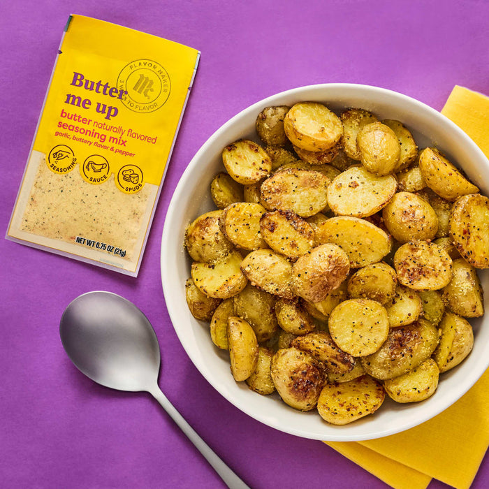 A bowl of roasted potatoes seasoned with Native Snax Butter Me Up seasoning blend is displayed next to the seasoning packet and a spoon.
