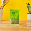 A package of Trader Joes Green Goddess seasoning blend is displayed on a wooden surface against a vibrant yellow background.