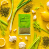 A packet of Trader Joes Green Goddess seasoning is surrounded by fresh ingredients like lemon garlic celery and green onions highlighting the products natural and flavorful composition.