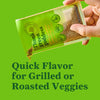 A hand pours the contents of a Thank Green Goddess seasoning packet highlighting its use for adding quick flavor to grilled or roasted vegetables.