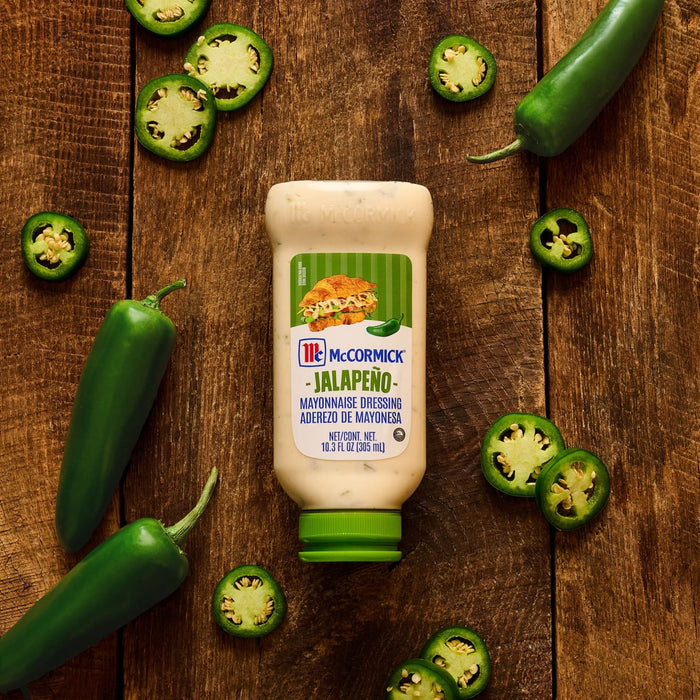 A bottle of McCormick Jalapeño Mayonnaise Dressing is displayed on a wooden surface surrounded by fresh whole and sliced jalapeños.