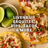 Three tostadas topped with a creamy salad and fresh salsa are arranged next to a small bowl of lime wedges beneath text stating it livens up esquites, dips, tacos and more.
