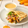 A grilled pita bread filled with chicken onions and cilantro is served on a white plate with a side of dipping sauce.