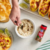 A hand stirs a bowl of dip next to McCormick Hatch Chile Pepper Crushed seasoning breakfast tacos and lime wedges.