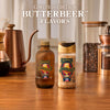 A bottle of McCormick Harry Potter Butterbeer Flavor and a shaker of McCormick Harry Potter Butterbeer Finishing Sugar are displayed on a wooden table.