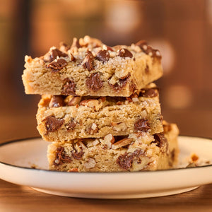 A stack of three chocolate chip cookie bars sits on a white plate, showcasing a sweet treat.