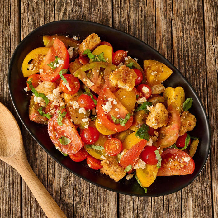 A fresh tomato and crouton panzanella salad, seasoned with Mccormick Grill Mates Bourbon &amp; Oak Seasoning Ground 3.37 Oz, is presented in a black bowl on a rustic wooden table.