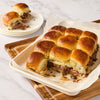 A tray of savory slider sandwiches with melted cheese and a side plate of the same.