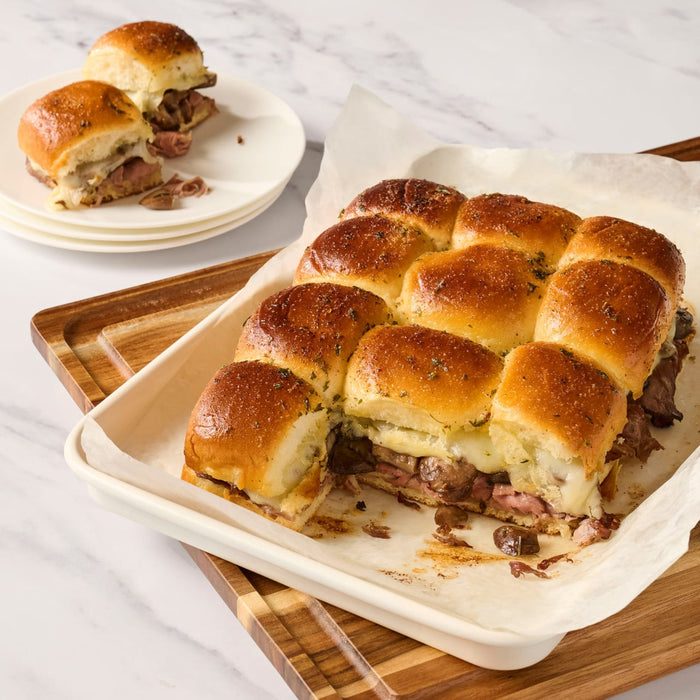 A tray of savory slider sandwiches with melted cheese and a side plate of the same.