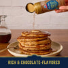 A hand sprinkles Mccormick Harry Potter Chocolate Frog Finishing Sugar, 3.47 Oz over a tall stack of pancakes drizzled with syrup to create a rich and chocolate-flavored breakfast.