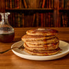 A stack of fluffy pancakes is topped with butter, drizzled with syrup, and sprinkled with Mccormick Harry Potter Chocolate Frog Finishing Sugar, 3.47 Oz for a magical breakfast.