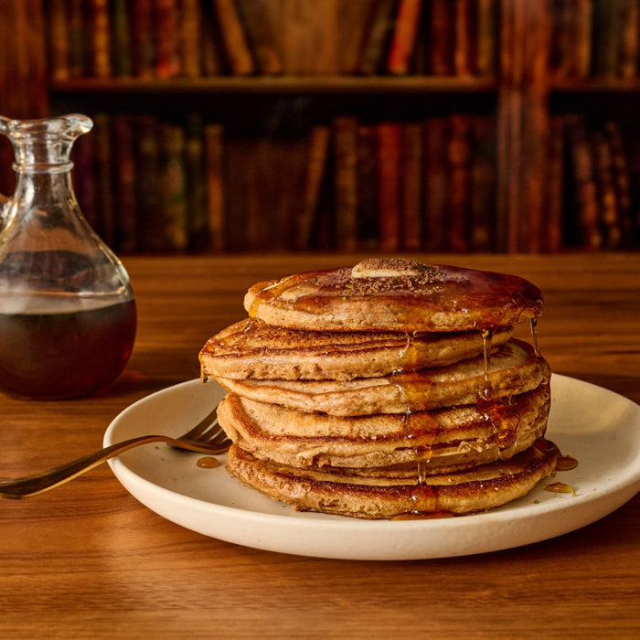 A stack of fluffy pancakes is topped with butter, drizzled with syrup, and sprinkled with Mccormick Harry Potter Chocolate Frog Finishing Sugar, 3.47 Oz for a magical breakfast.