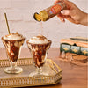 A hand sprinkles Mccormick Harry Potter Cauldron Cake Finishing Sugar, 3.43 Oz over two chocolate sundaes in a Harry Potter-themed setting.