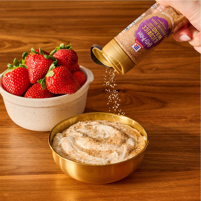 A hand sprinkles Mccormick Harry Potter Licorice Wand Finishing Sugar, 3.39 Oz onto a creamy dip served with a side of fresh strawberries.