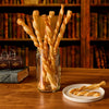 Twisted pastry wands are sprinkled with Mccormick Harry Potter Licorice Wand Finishing Sugar, 3.39 Oz and arranged in a jar on a wooden desk in front of a bookshelf.