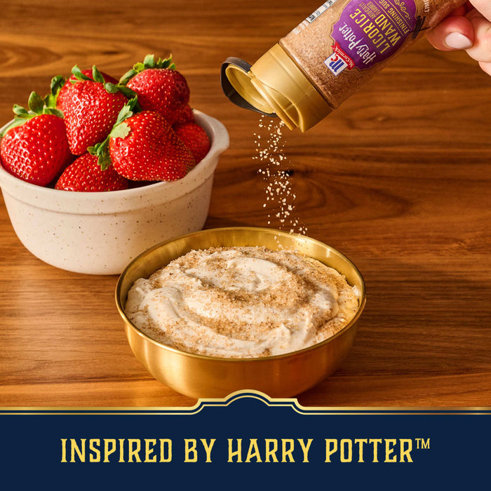 A hand sprinkles Mccormick Harry Potter Licorice Wand Finishing Sugar, 3.39 Oz, onto a creamy dip in a golden bowl, with a side of fresh strawberries.