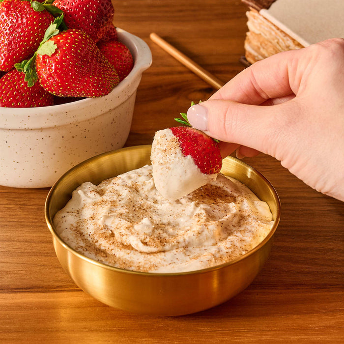 A hand dips a fresh strawberry into a bowl of creamy fruit dip that has been sprinkled with Mccormick Harry Potter Licorice Wand Finishing Sugar, 3.39 Oz.