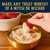 A hand dips a strawberry into a bowl of creamy dip sprinkled with Mccormick Harry Potter Licorice Wand Finishing Sugar, 3.39 Oz, to create a magical treat.