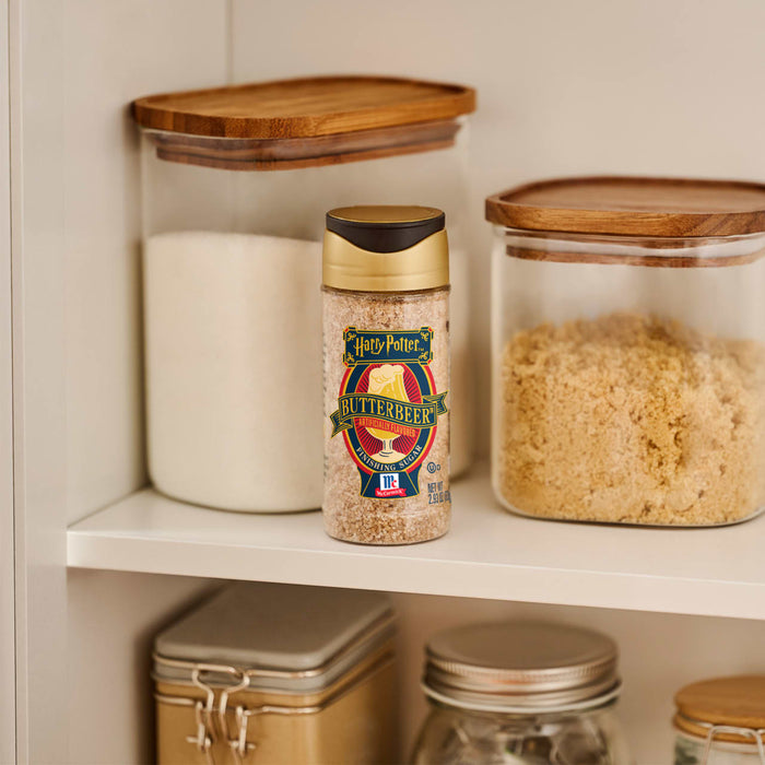 A bottle of Harry Potter Butterbeer Artificially Flavored Finishing Sugar by McCormick sits on a shelf among jars of sugar.
