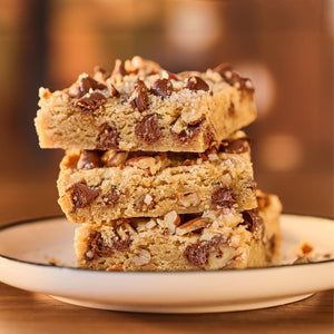 A stack of three chocolate chip cookie bars with nuts sits on a white plate.