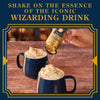 A hand shakes Harry Potter Butterbeer shimmer topping onto mugs of whipped cream, suggesting a magical beverage experience.