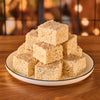 A stack of homemade rice crispy treats sits on a white plate with a black rim, set on a wooden table against a blurred background.