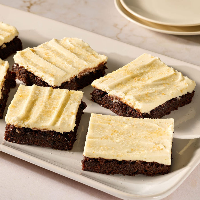 A white serving platter holds several rich chocolate brownies topped with a thick layer of frosting made from Mccormick Salted Caramel Cheesecake Seasoning Mix 1.62 Oz and a sprinkle of coarse sugar.