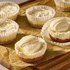 Miniature cheesecakes with a graham cracker crust and creamy topping are prepared using Mccormick Salted Caramel Cheesecake Seasoning Mix 1.62 Oz on a parchment lined wooden board.