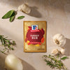 A package of Mccormick Turkey Rub, 1.25 Oz is displayed on a stone surface surrounded by fresh ingredients like whole garlic bulbs, a white onion, and sprigs of rosemary, sage, and thyme.