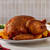 A golden brown roasted turkey seasoned with Mccormick Turkey Rub, 1.25 Oz is presented on a white platter garnished with orange slices and cranberries.