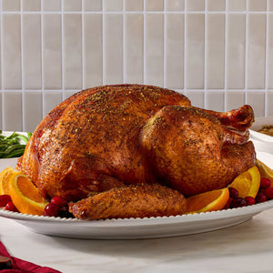 A golden brown roasted turkey seasoned with Mccormick Turkey Rub, 1.25 Oz is presented on a white platter garnished with orange slices and cranberries.