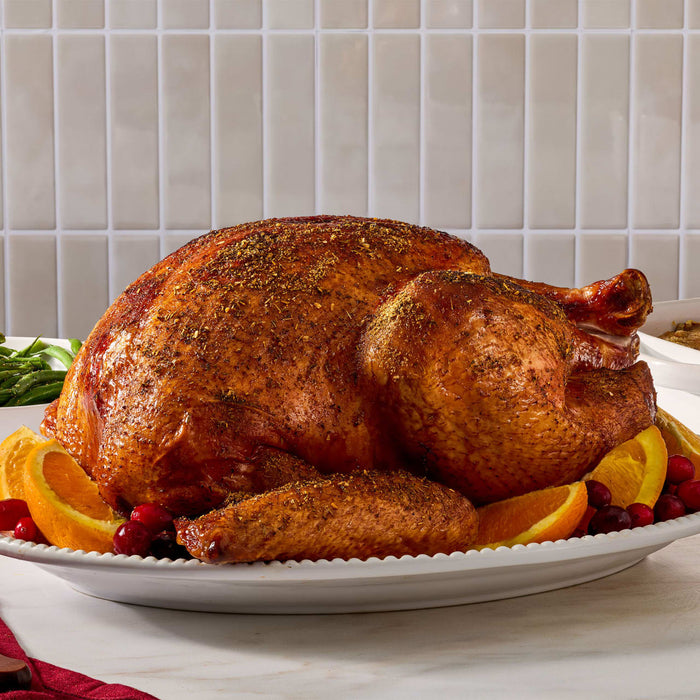 A golden brown roasted turkey seasoned with Mccormick Turkey Rub, 1.25 Oz is presented on a white platter garnished with orange slices and cranberries.