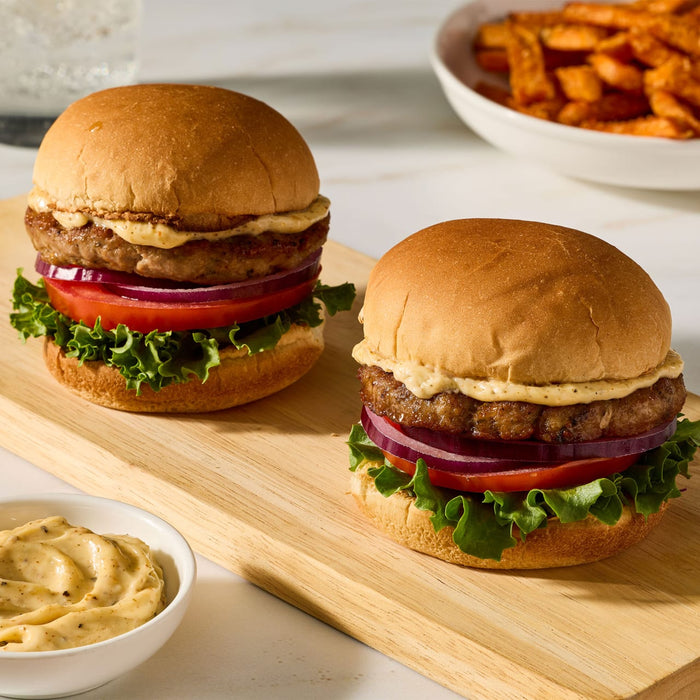Two juicy turkey burgers seasoned with Mccormick Turkey Rub 1.25 Oz are served on a wooden board with lettuce tomato red onion and a side of sweet potato fries.