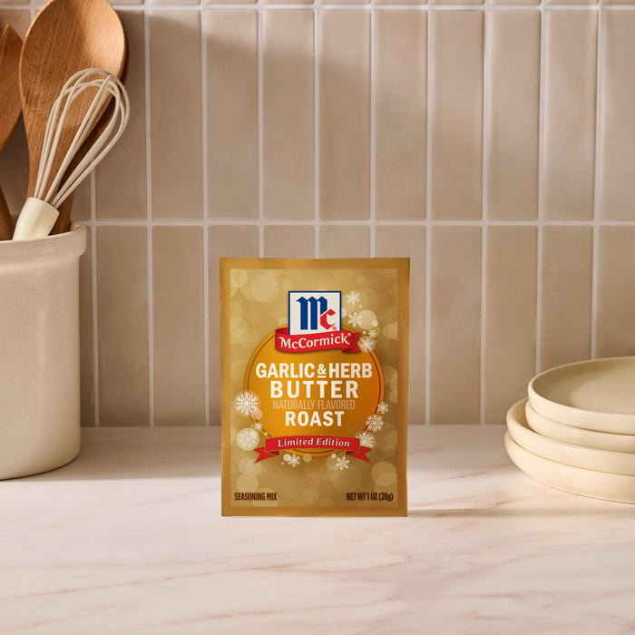 A package of Mccormick Garlic And Herb Butter Roast Seasoning Mix, 1.0 Oz stands on a marble countertop in a kitchen setting with wooden utensils and white plates.