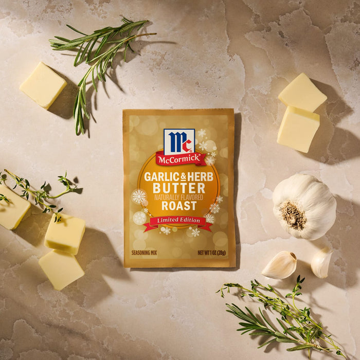 A package of Mccormick Garlic And Herb Butter Roast Seasoning Mix, 1.0 Oz is displayed on a stone surface surrounded by fresh garlic cloves, sprigs of rosemary and thyme, and pats of butter.