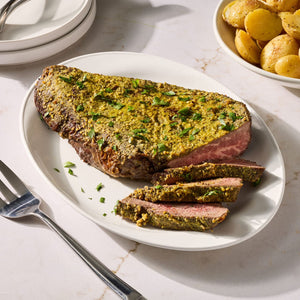 A succulent beef roast is sliced on a white platter and coated in a savory crust made with Mccormick Garlic And Herb Butter Roast Seasoning Mix 1.0 Oz alongside a bowl of roasted potatoes.