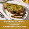 A sliced beef roast topped with a vibrant green crust prepared using Mccormick Garlic And Herb Butter Roast Seasoning Mix 1.0 Oz is presented on a white platter alongside roasted potatoes.