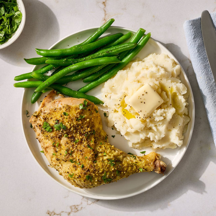 A roasted chicken leg seasoned with Mccormick Garlic And Herb Butter Roast Seasoning Mix, 1.0 Oz is served on a plate with mashed potatoes and green beans.