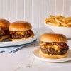 Three juicy bacon cheeseburgers topped with caramelized onions and seasoned with Mccormick Garlic And Herb Butter Roast Seasoning Mix 1.0 Oz are served alongside a bowl of thick cut fries.