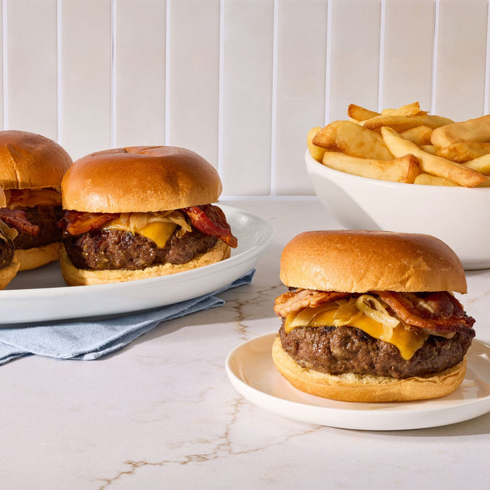 Three juicy bacon cheeseburgers topped with caramelized onions and seasoned with Mccormick Garlic And Herb Butter Roast Seasoning Mix 1.0 Oz are served alongside a bowl of thick cut fries.
