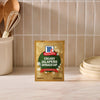 A package of Mccormick Creamy Jalapeno Spinach Dip Seasoning Mix, 0.87 Oz stands on a marble countertop in a kitchen setting with wooden utensils and plates in the background.