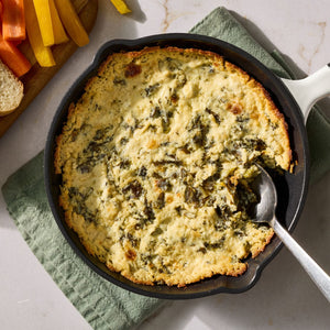 A cast iron skillet holds a warm and bubbly appetizer prepared with Mccormick Creamy Jalapeno Spinach Dip Seasoning Mix 0.87 Oz served alongside fresh vegetable sticks and bread.