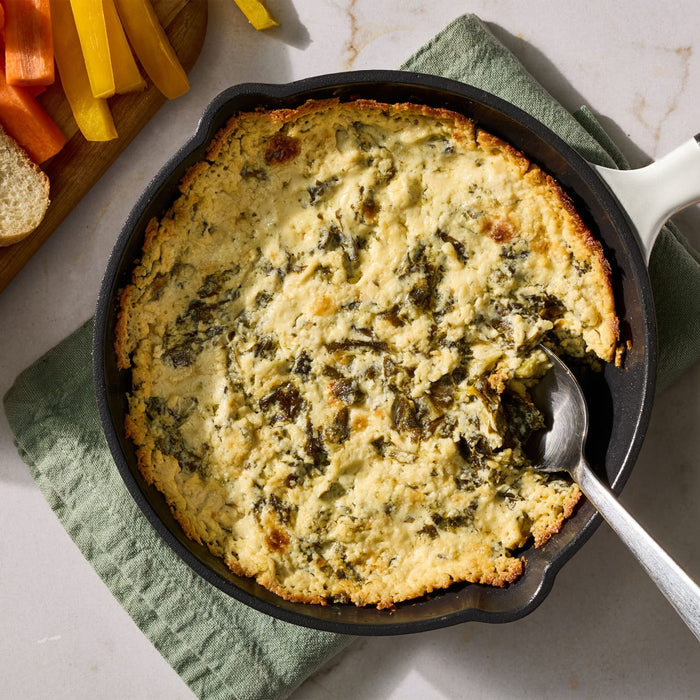 A cast iron skillet holds a warm and bubbly appetizer prepared with Mccormick Creamy Jalapeno Spinach Dip Seasoning Mix 0.87 Oz served alongside fresh vegetable sticks and bread.