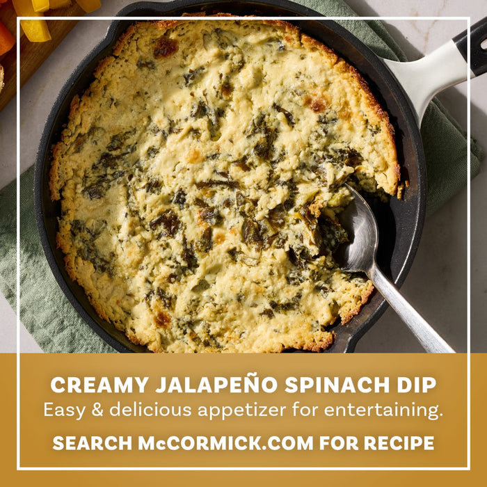 A cast iron skillet filled with a bubbly and golden brown appetizer made using Mccormick Creamy Jalapeno Spinach Dip Seasoning Mix 0.87 Oz is shown with a serving spoon and fresh bell peppers on the side.