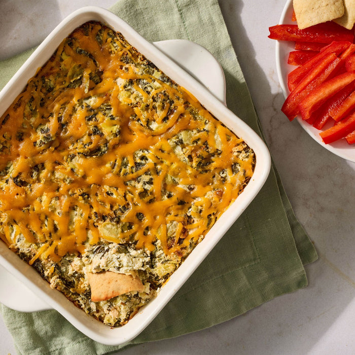 A warm and bubbly spinach and artichoke appetizer prepared with Mccormick Creamy Jalapeno Spinach Dip Seasoning Mix 0.87 Oz is served in a white baking dish alongside fresh red pepper strips and tortilla chips.
