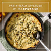 A golden brown skillet of baked appetizer made with Mccormick Creamy Jalapeno Spinach Dip Seasoning Mix 0.87 Oz is served with a spoon and fresh vegetables.