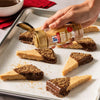 A hand sprinkles Mccormick English Toffee Finishing Sgr 3.7 Oz onto a pan of glazed cinnamon rolls.