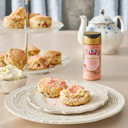 A plate of scones with cream and McCormick Strawberry Extract next to a tiered serving tray and teapot.